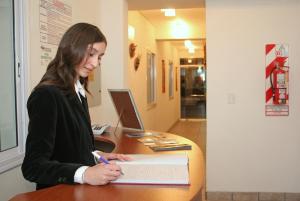 una mujer sentada en un escritorio escribiendo en un libro en Wilson Apart Hotel en Salta