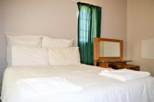 cama blanca con cortina verde y espejo en Malolotja Log Cabins en Mbabane