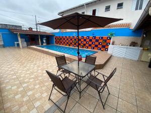 una mesa con sillas y una sombrilla junto a la piscina en Casa com Piscina e Churrasqueira, en Praia Grande