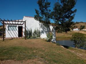 Casa de Campo Recanto Têto في إسبيريتو سانتو دو بينهال: مبنى ابيض صغير فيه شجرة بجانب بحيرة