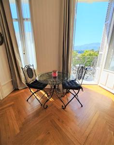 Una mesa de cristal y 2 sillas en una habitación con balcón. en Grand studio 38m2 dans ancien palace avec piscine et place de parking privée en Aix-les-Bains