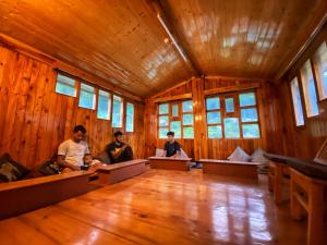 un grupo de personas sentadas en una gran habitación con paredes de madera en Pine Tower Inn, en Manali