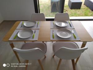 uma mesa de madeira com quatro cadeiras e pratos em Taghazout bay - Tawenza Medina - Apt avec piscine partagée et Jardin em Tamraght Ouzdar