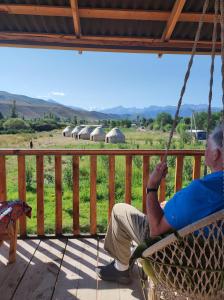 Um homem mais velho sentado num baloiço a olhar para um campo. em Eco Village Lodge em Dzhetyoguz