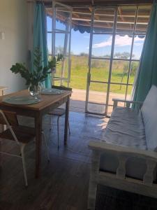 una sala de estar con mesa y sofá y una habitación con ventana en Uy - ROMÁNTICA Cabaña en entorno Natural único en Mercedes