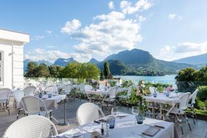 un restaurant avec des tables et des chaises blanches et un lac dans l'établissement Hôtel Beau Site Talloires B SPA, à Talloires