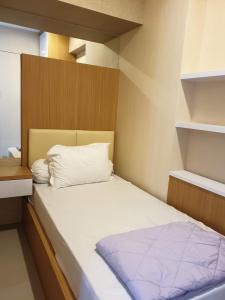 a small bedroom with a bed and shelves at Cosmy Tanglin Apartment in Surabaya
