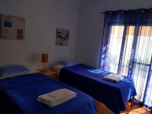two beds in a room with blue sheets and a window at Comporta beach house in Carvalhal