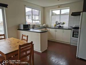 a kitchen with white cabinets and a table and a refrigerator at White weather board house in Auckland