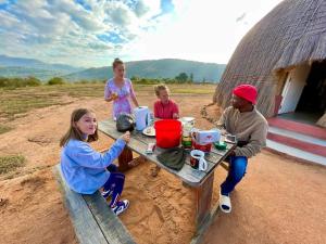 a group of people sitting at a table in front of a hut at Swazi Dreams. (Nqabaneni Eco-Volunteering.) in Usutu