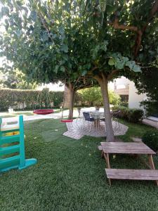 einen Park mit zwei Bänken und einem Tisch unter einem Baum in der Unterkunft Galini apartment near sea, port and airport in Artemida