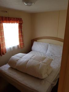 a bedroom with a white bed with a window at PG49 8 BERTH PET FRIENDLY CARAVAN GOLDEN PALM in Chapel Saint Leonards