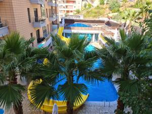 a yellow pool with palm trees in front of a building at Black'n White Apartment in Vlorë