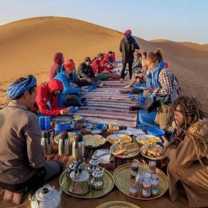 Eine Gruppe von Menschen, die an einem Tisch in der Wüste sitzen in der Unterkunft Moha House in Merzouga