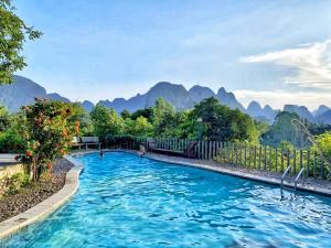 una piscina de agua azul con montañas al fondo en Riverside Retreat Hotel, en Yangshuo