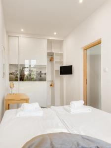 a white bedroom with two white beds and a tv at COCO Apartments Gdańsk Centrum Górka in Gdańsk