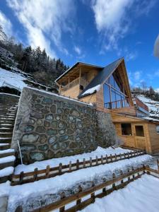 a log cabin in the snow with a stone wall at OTANİ DAĞ EVLERİ in Çamlıhemşin