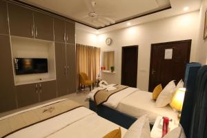Una habitación de hotel con dos camas y un televisor. en Cuzzy Inn Hotel, en Lahore