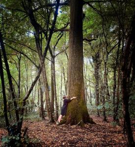 una mujer apoyada en un árbol en el bosque en Maison d'hôtes chez Aud, en Dagneux
