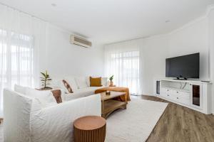 a white living room with a white couch and a tv at Seascape at The Cape in Cape Paterson