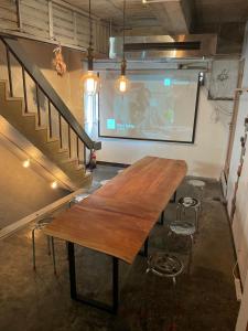 una mesa de madera en una habitación con pantalla de proyección en Beppu hostel&cafe ourschestra, en Beppu