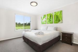 a white bedroom with a large bed and a window at Romantic lakehouse set in a private vineyard in the Hunter Valley in Lovedale