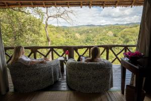 Dos chicas sentadas en sillas en un porche con vistas en Sable Mountain Lodge, A Tent with a View Safaris, en Kisaki