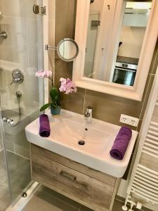 La salle de bains est pourvue d'un lavabo, de serviettes violettes et d'un miroir. dans l'établissement Hues-Stroongoedj-Haus-Strandgut, à Westerland