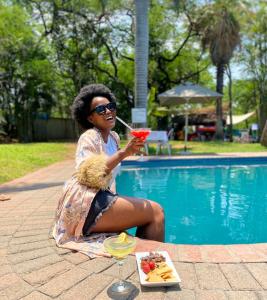 una mujer sentada junto a una piscina sosteniendo una bebida en Sefapane Lodge and Safaris, en Phalaborwa