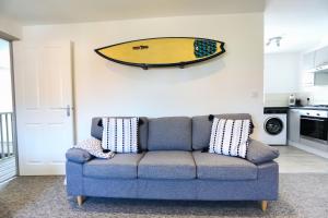 a living room with a blue couch with a surfboard on the wall at Shorebreak - Bracklesham Bay Apartment in Chichester