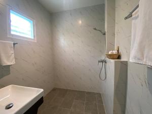 ein weißes Bad mit einem Waschbecken und einer Dusche in der Unterkunft Le Petit Saint Tropez in Khanom