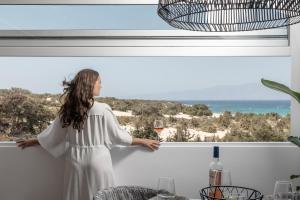 Una donna con un vestito bianco che guarda fuori da una finestra di Ammolofos Luxury Apartment & suites a Naxos Chora