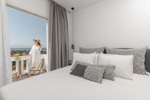 a woman in a hotel room with a bed and a window at Ammolofos Luxury Apartment & suites in Naxos Chora