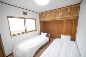 two beds in a room with white sheets at Tomoeドットコム3 in Hakodate