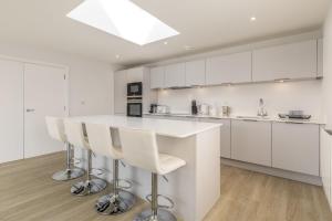 a kitchen with white cabinets and a bar with stools at 8 Challacombe - Luxury Apartment at Byron Woolacombe, only 4 minute walk to Woolacombe Beach! in Woolacombe