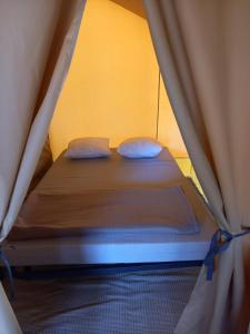 a bed in a tent with two pillows on it at Camping Onlycamp Le Petit Bocage in Les Essarts