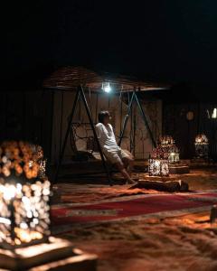 un homme assis dans une chaise sous un auvent la nuit dans l'établissement Bivouac ZAGORA, à Zagora