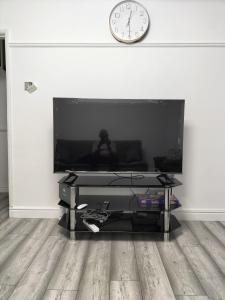 a living room with a television and a clock on a wall at Remaj Service Accommodation, Sleep 7 in Dagenham