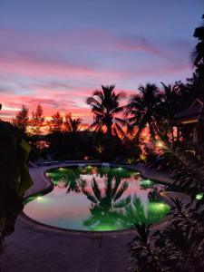 a pool with green lights in front of a sunset at RED PEARL BEACH RESORT in Chaloklum