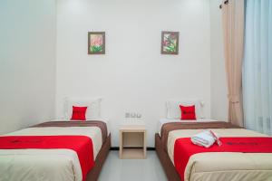 two beds in a room with red pillows at RedDoorz Plus Syariah @ Jalan Dokter Wahidin Bojonegoro in Bojonegoro
