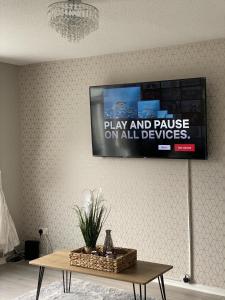 een flatscreen-tv hangend aan een muur boven een tafel bij Bv Luxury Spacious 3 Bedroom House At Isaac Close in Manchester