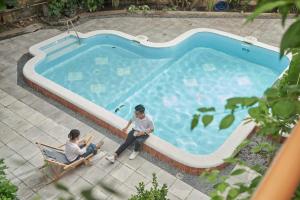 two men sitting in chairs next to a swimming pool at M Village The Tropic in Ho Chi Minh City