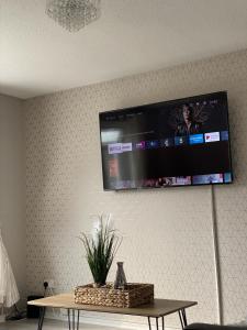 een tv aan een muur met een tafel met een plant bij Bv Luxury Spacious 3 Bedroom House At Isaac Close in Manchester
