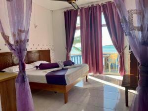 a bedroom with a bed with purple curtains and a window at Coco Villa in Mahébourg