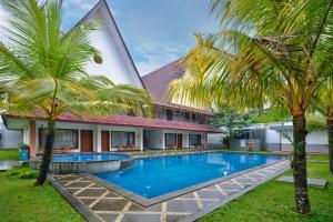 a swimming pool in front of a house with palm trees at Hadipriyanto Homestay in Banyumas