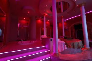 Alcova Suite&Relax في إبولي: غرفة مع إضاءة وردية وسرير وحوض استحمام