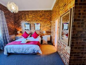 a bedroom with a bed with red pillows and a brick wall at Dullstroom Manor Game & Trout Lodge in Dullstroom