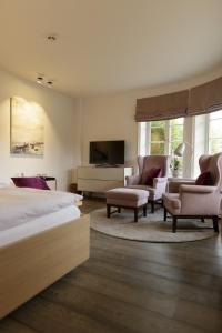 een slaapkamer met een bed en twee stoelen en een televisie bij Hotel Aarnhoog in Keitum