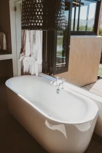 La salle de bains est pourvue d'une baignoire blanche et d'une fenêtre. dans l'établissement De Uijlenes, à Gansbaai