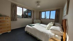 a bedroom with a bed and a dresser and windows at Kakariki by the sea in Ngunguru